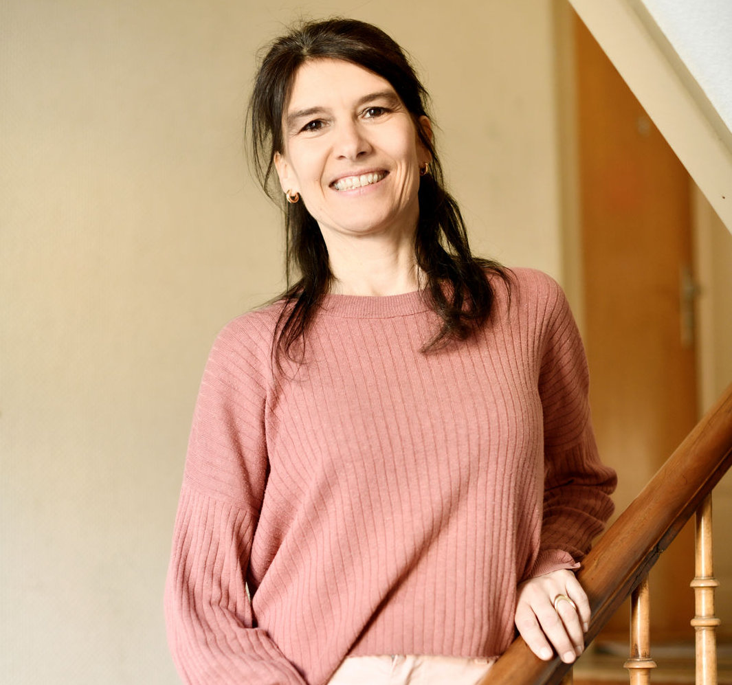 Portrait von der Kinesiologin Pascale Hauser. Sie steht im Treppenhaus und schaut lächelnd in die Kamera